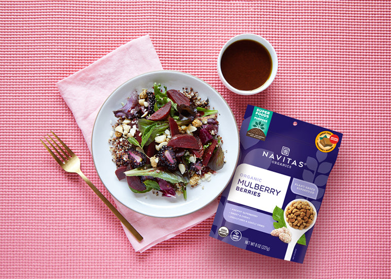 A bowl of salad mixed with beets and Navitas Organics Mulberries, aside a dish filled with dressing made with Navitas Organics Vanilla & Greens Essential Blend Protein Powder