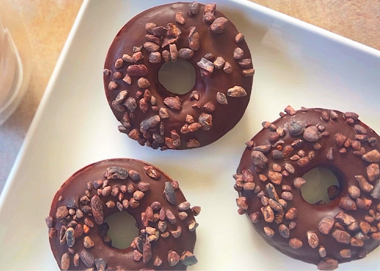 Three chocolate donuts made with Navitas Organics Cacao Butter Wafers, Cacao Wafers and Cacao Sweet Nibs