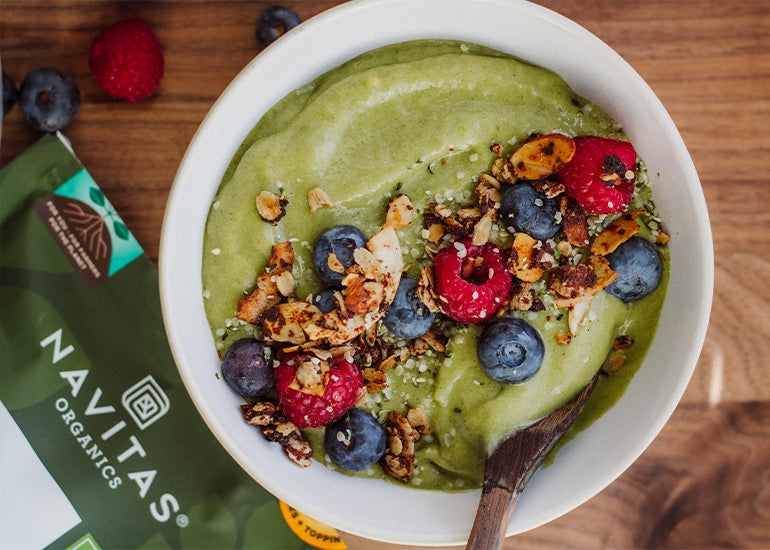 A creamy green smoothie bowl made with Navitas Organics Superfood+ Greens Blend and Hemp Powder, topped with Navitas Organics Hemp Seeds, fresh berries and granola.
