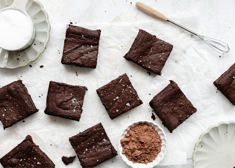 Dairy and grain-free fudge brownies made with Navitas Organics Cacao Wafers and Cacao Powder spread out on parchment paper.