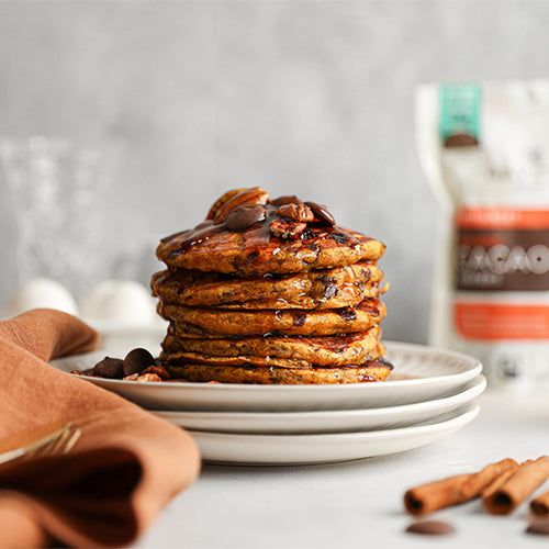 Pumpkin chocolate chunk pancakes made with Navitas Organics Semi-sweet Cacao Wafers, topped with maple syrup and chopped nuts.