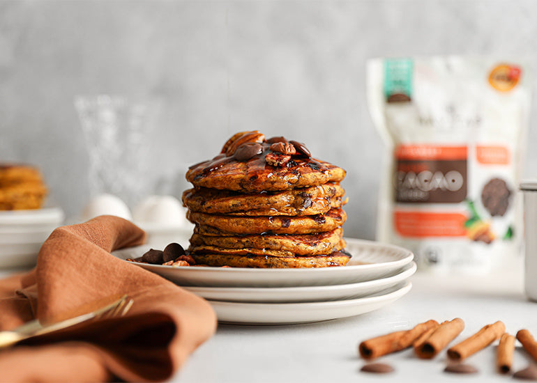 Pumpkin chocolate chunk pancakes made with Navitas Organics Semi-sweet Cacao Wafers, topped with maple syrup and chopped nuts.