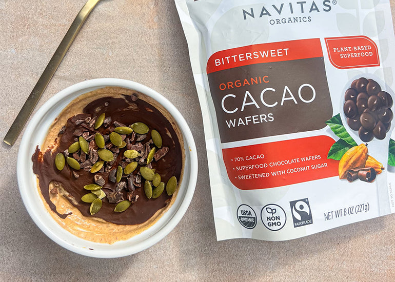 A pumpkin yogurt cup covered with a chocolate layer made with Navitas Organics Bittersweet Cacao Wafers, with pepitas and Navitas Organics Cacao Nibs sprinkled on top.