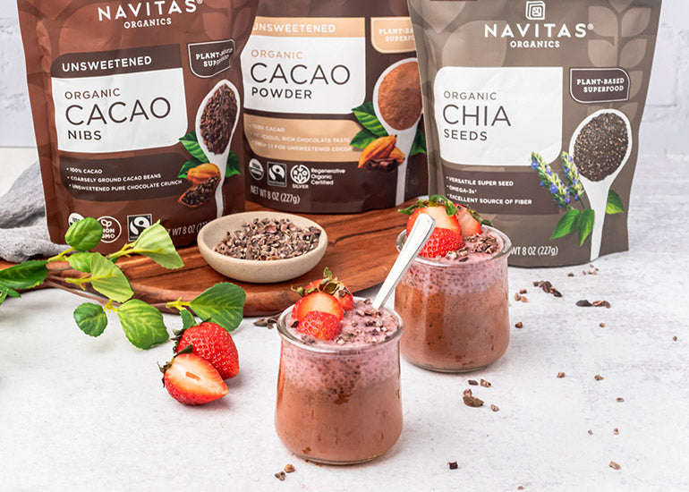 Two cups of chocolate strawberry chia pudding made with Navitas Organics Cacao Powder and Chia Seeds, topped with fresh strawberries and Navitas Organics Cacao Nibs.