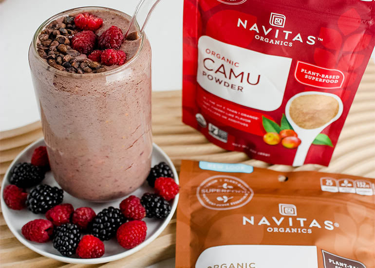 A fruity, chocolatey smoothie made with Navitas Organics Cacao Powder and Camu Powder, in a tall serving glass, topped with Navitas Organics Cacao Sweet Nibs and fresh berries