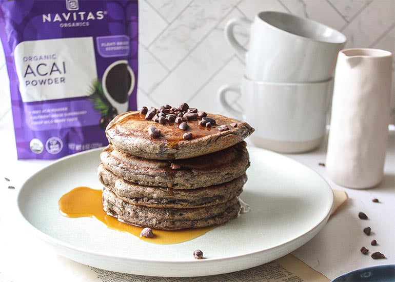 A stack of gluten-free acai pancakes made with Navitas Organics Acai Powder, topped with maple syrup and Navitas Organics Cacao Nibs
