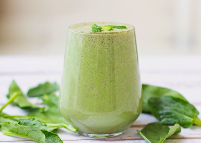 A green smoothie made with Navitas Organics Hemp Seeds and Chia Seeds in a glass, surrounded by mint leaves.