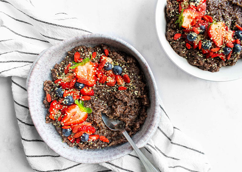 Two bowls filled with acai rice pudding made with Navitas Organics Acai Powder, topped with fresh berries, and Navitas Organics Goji Berries and Hemp Seeds