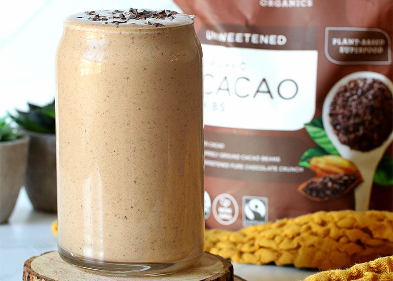 A chocolate peanut butter protein shake in a tall glass topped with Navitas Organics Cacao Nibs