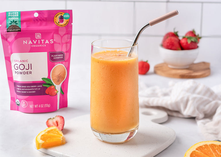 A bright orange tropical smoothie made with Navitas Organics Goji Berry Powder in a tall glass with a straw