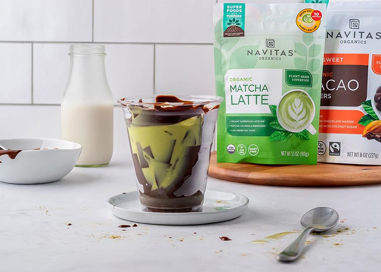 A crackling chocolate iced matcha latte made with Navitas Organics Instant Matcha Latte Mix and Semi-sweet Cacao Wafers in a plastic cup on a plate