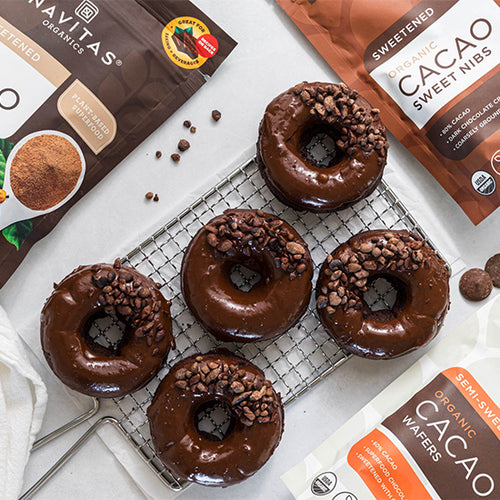 A cooling rack topped with five chocolate donuts made with Navitas Organics Cacao Powder, coated in a glaze made with Navitas Organics Semi-sweet Cacao Wafers and sprinkled with Navitas Organics Cacao Sweet Nibs
