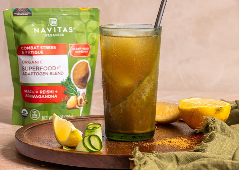 A tall glass filled with an adaptogenic cucumber spritz mocktail drink on a tray next to a bag of Navitas Organics Superfood+ Adaptogen Blend
