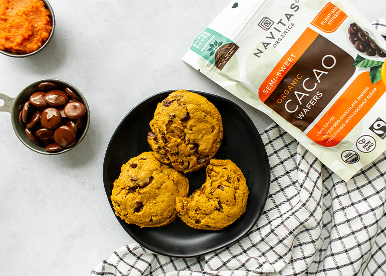 A plate of pumpkin spice cookies next to a bag of Navitas Organics Semi-sweet Cacao Wafers, a dish filled with cacao wafers and a dish filled with pumpkin puree
