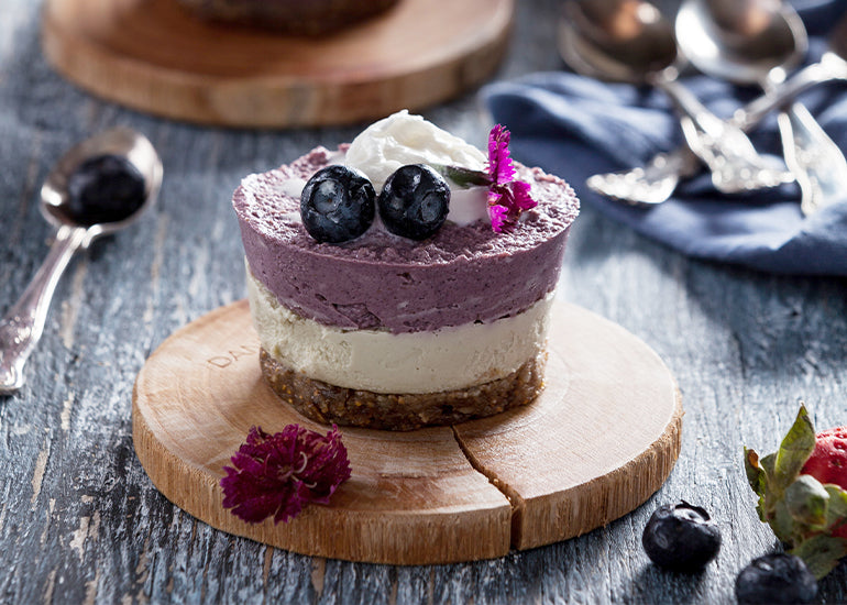 A blueberry maqui cheesecake made with Navitas Organics Cacao Powder and Maqui Powder sitting on a wooden board.