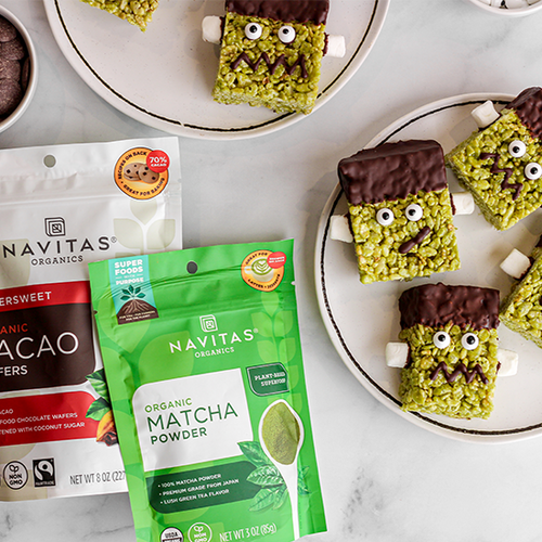 Plate of square, green matcha-flavored treats decorated to look like monsters with eyes and teeth, next to packages of Navitas Organics Bittersweet Cacao Wafers and Matcha Powder.