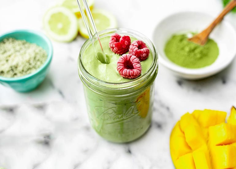 Green smoothie topped with frozen raspberries, made with Navitas Organics Vanilla & Greens Essential Blend and Matcha Powder