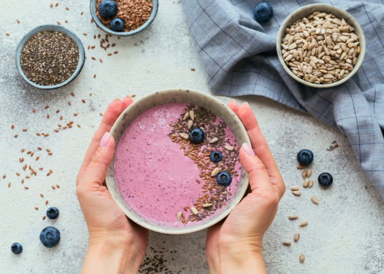 A woman holding a smoothie bowl topped with fresh blueberries and Navitas Organics Chia Seeds.