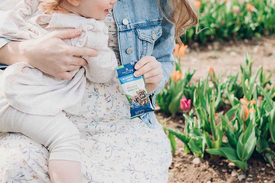 A mother holding her daughter with Navitas Organics Blueberry Hemp Power Snacks in a garden