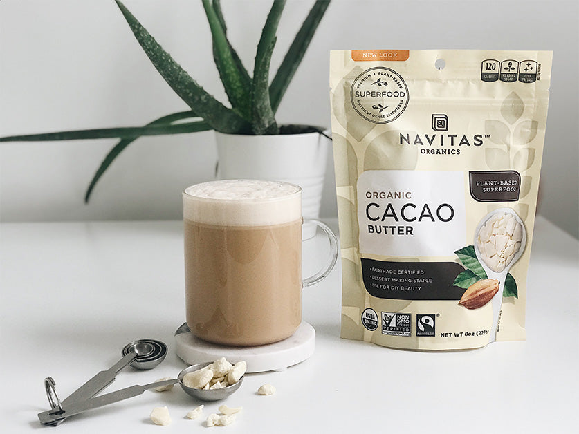A latte made with Navitas Organics Cacao Butter and a bag of product with a scoop of chopped Cacao Butter