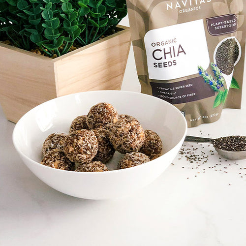 A bowl of chia bites made with Navitas Organics Chia Seeds in front of a plant, a bag of chia seeds and a scoop filled with chia seeds