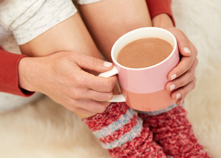 A woman in sweatpants and cozy socks holding a hot cocoa made with Navitas Organics Cacao Powder