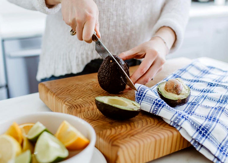 Yoga Teacher and Wellness Blogger Helene Kusman in her kitchen cutting an avocado in half.