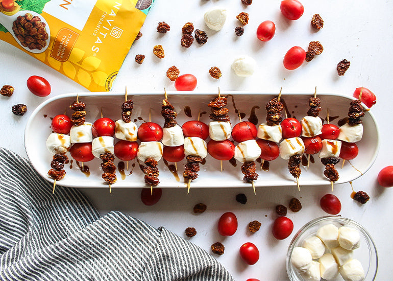 A platter of goldenberry caprese bites made with grape tomatoes, mozzarella cheese and Navitas Organics Goldenberries, drizzled with a balsamic glaze, surrounded by scattered tomatoes, cheese and goldenberries 