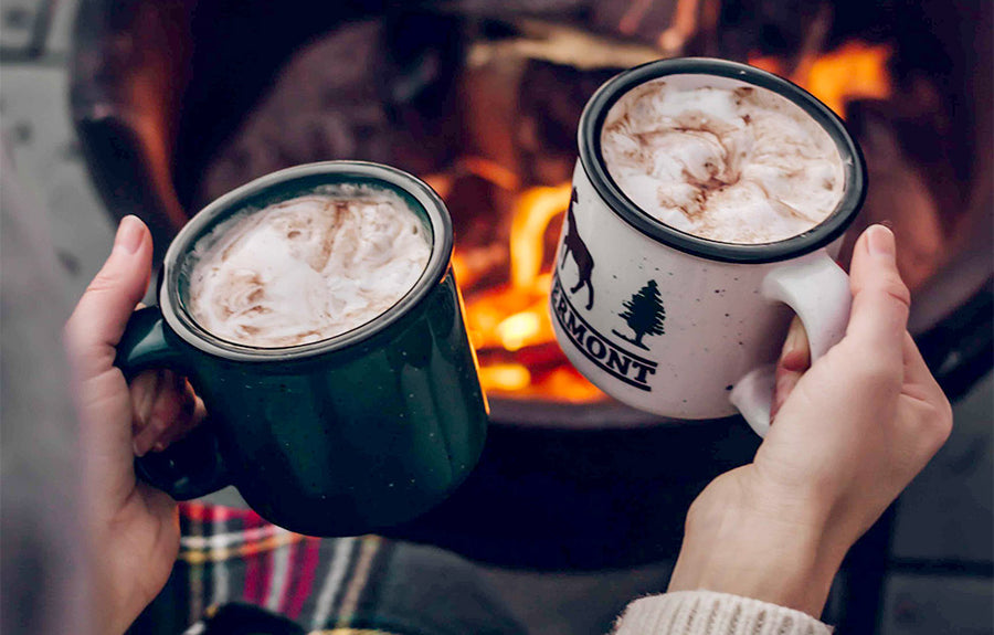 Two people toasting with hot chocolate in front of a fireplace