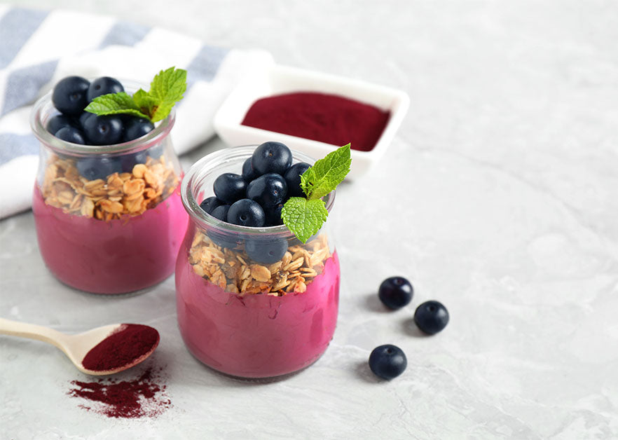 Yogurt cups mixed with Navitas Organics Acai Powder, topped with oats, blueberries and mint