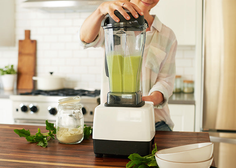 A woman making a smoothie in a blender with Navitas Organics superfood ingredients.