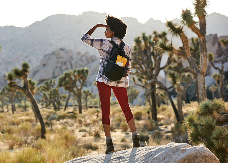 A woman standing on a rock with a backpack full of Navitas Organics Goldenberries in the California desert.