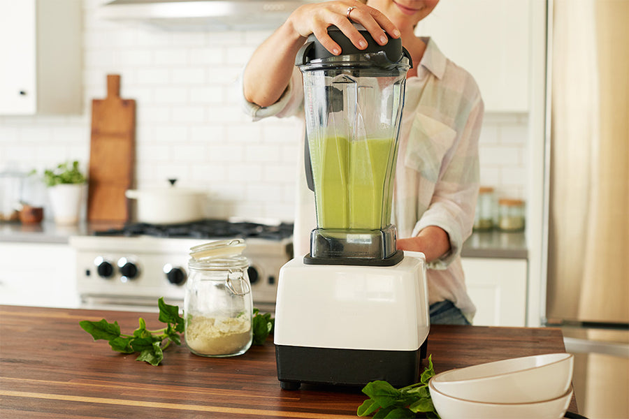A woman blending a green smoothie with Navitas Organics detox-friendly superfoods.