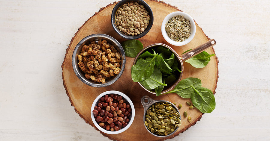 Various plant-based sources of iron, including Navitas Organics Mulberries, Hemp Seeds, and others, in bowls on a wooden board.
