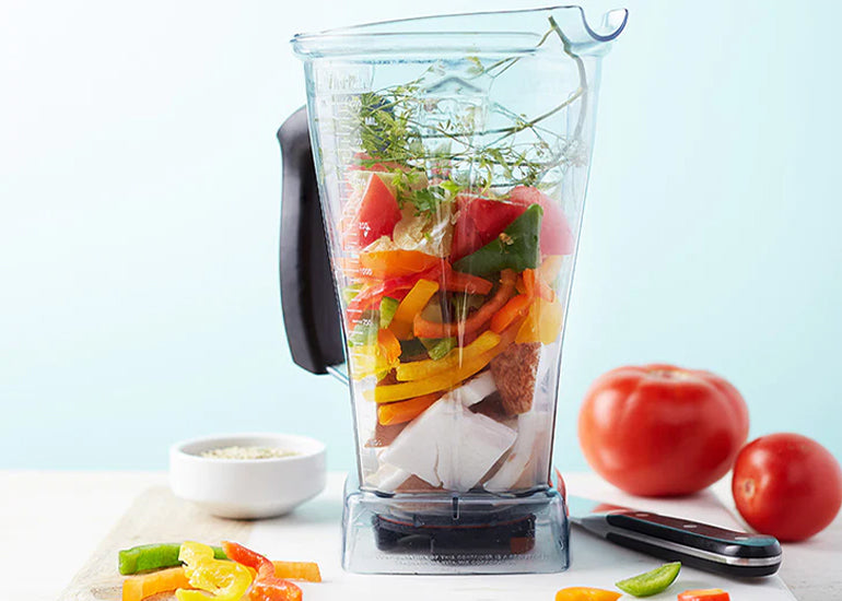 A blender filled with fresh vegetables on a kitchen counter.