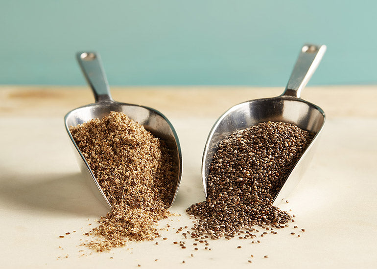 A scoop of Navitas Organics Chia Powder next to a scoop of Navitas Organics Chia Seeds