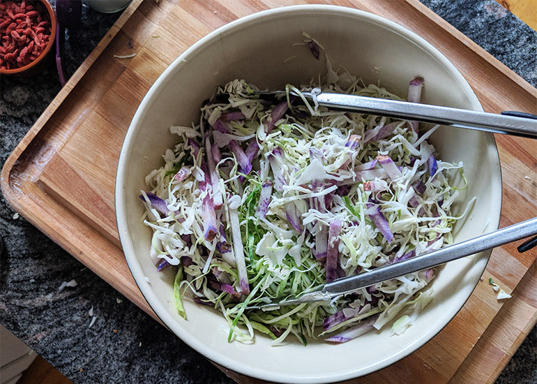 Fermented vegetables in a bowl with tongs on a wooden cutting board
