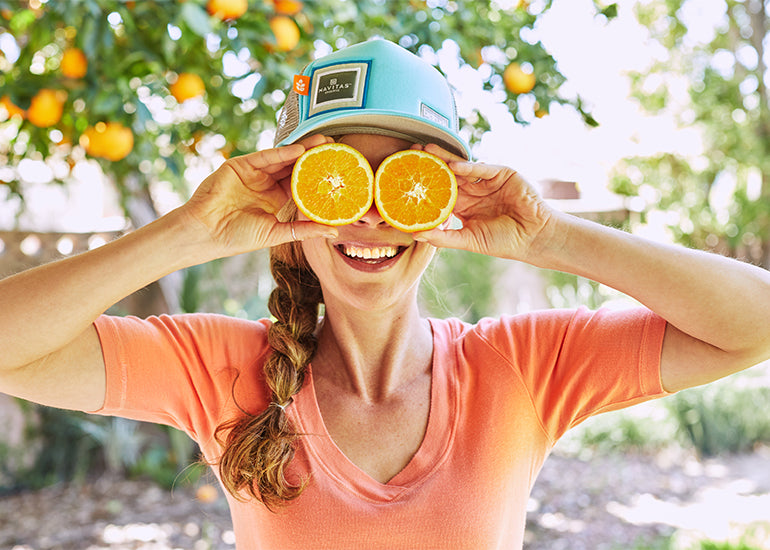 A woman smiling while holding orange slices over her eyes