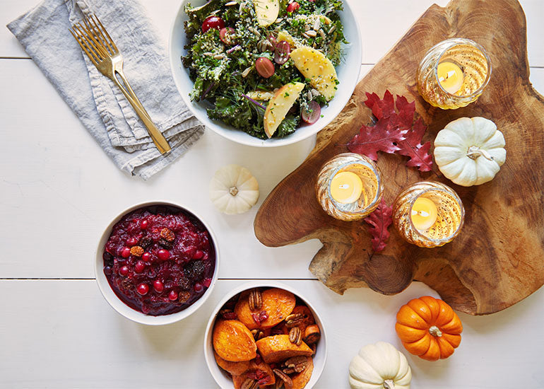 A fall holiday table spread with root vegetables, cranberry sauce, a salad, and candles.