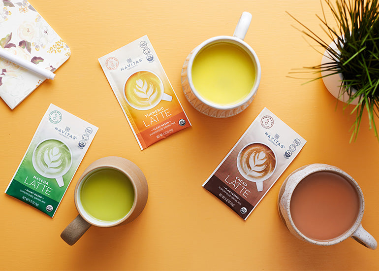 Navitas Organics Superfood Latte Mixes alongside mugs of their prepared corresponding lattes.