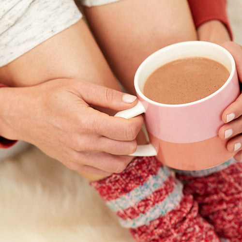 A woman in cozy socks and sweatpants holding a mug filled with hot cocoa made with Navitas Organics Cacao Powder