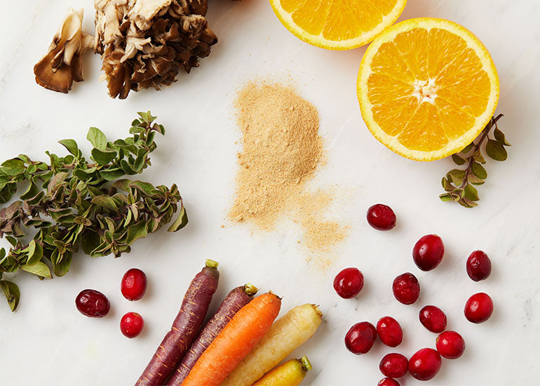 A pile of Navitas Organics Camu Powder surrounded by oranges, carrots, camu berries, and other nutrient-rich whole foods.