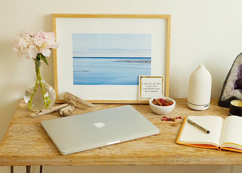 A desk with a laptop, notebook, flowers, and a bowl of Navitas Organics Goji Berries.