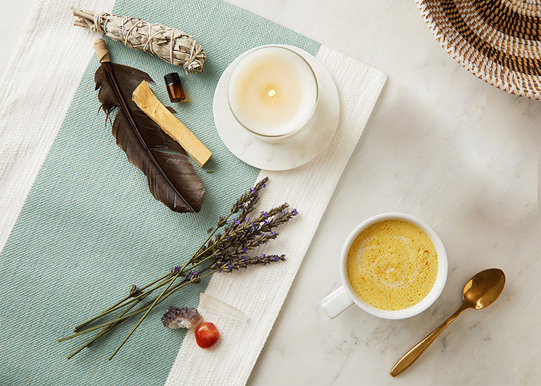 A turmeric latte, lit candle and sage on a marble table.