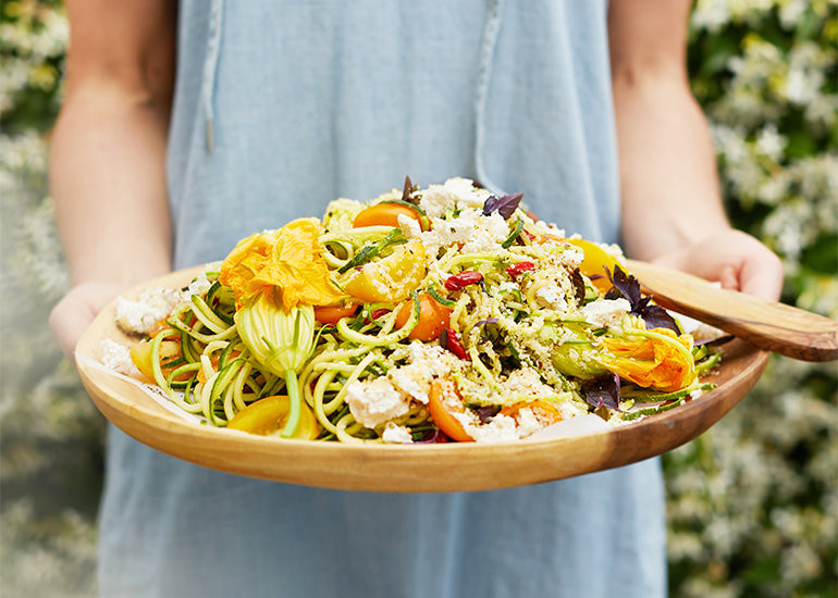 A woman holding a platter of spiralized veggies topped with Navitas Organics Hemp Seeds.