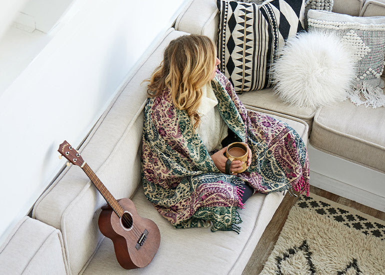 A woman wrapped in a blanket on a couch holding a superfood hot drink 