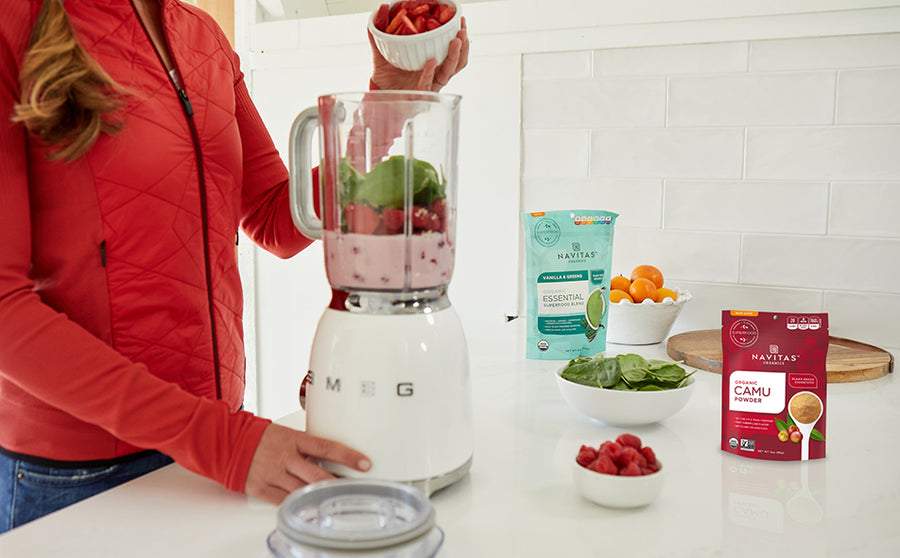 Woman in kitchen adding fresh berries to a blender full of Navitas Organics superfoods and other smoothie ingredients
