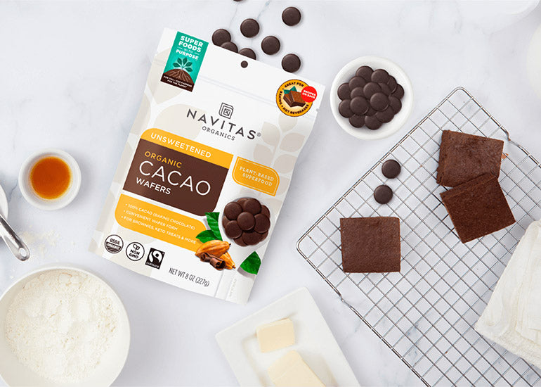 A bag of Navitas Organics Fairtrade Certified Cacao Wafers spilling out onto a countertop next to a cooling rack with brownies.