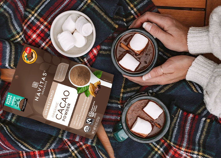 A woman holding hot chocolate made with Navitas Organics Cacao Powder, topped with marshmallows