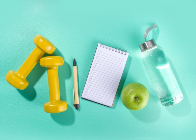 Dumbbells, a notebook and pen, an apple and a water bottle.
